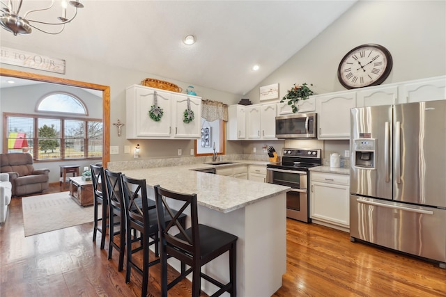 kitchen with appliances with stainless steel finishes, white cabinets, a sink, wood finished floors, and a peninsula