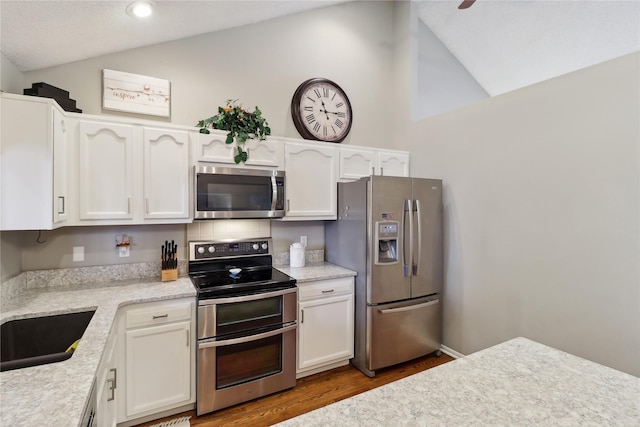 kitchen with stainless steel appliances, wood finished floors, a sink, white cabinets, and vaulted ceiling