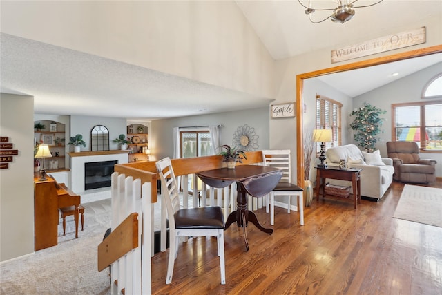 dining room with vaulted ceiling, wood finished floors, a textured ceiling, and a glass covered fireplace