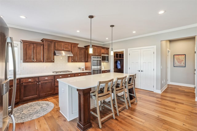 kitchen featuring light countertops, backsplash, appliances with stainless steel finishes, light wood-type flooring, and under cabinet range hood