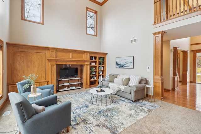 carpeted living room with a towering ceiling, ornate columns, baseboards, and visible vents