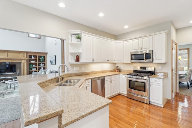 kitchen with white cabinets, appliances with stainless steel finishes, a peninsula, open shelves, and a sink