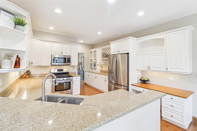 kitchen with light stone counters, stainless steel appliances, open shelves, a sink, and recessed lighting