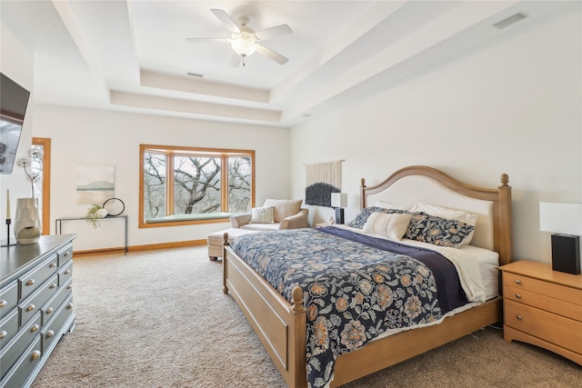 carpeted bedroom featuring a tray ceiling, a ceiling fan, visible vents, and baseboards