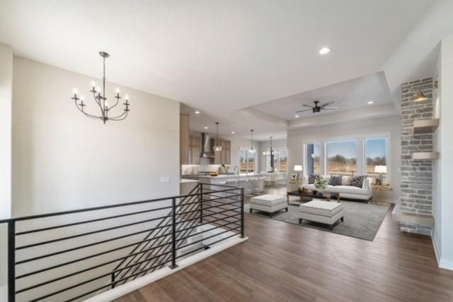 living room featuring ceiling fan with notable chandelier, a tray ceiling, recessed lighting, and wood finished floors