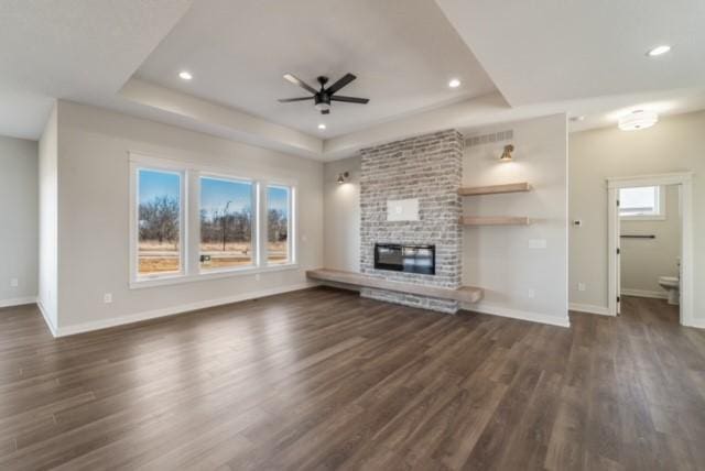 unfurnished living room with dark wood-style floors, baseboards, a fireplace, and a tray ceiling