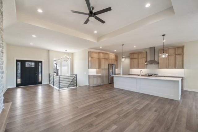 kitchen featuring dark wood-style flooring, open floor plan, light countertops, wall chimney range hood, and a raised ceiling