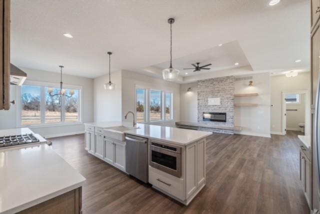 kitchen with a fireplace, stainless steel appliances, a raised ceiling, light countertops, and a sink