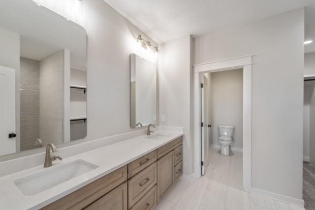 full bath with baseboards, a sink, toilet, and double vanity