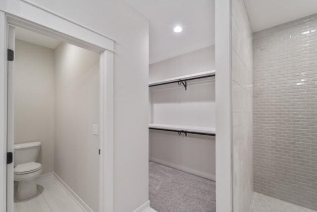 bathroom featuring a walk in closet, recessed lighting, toilet, tile patterned flooring, and baseboards