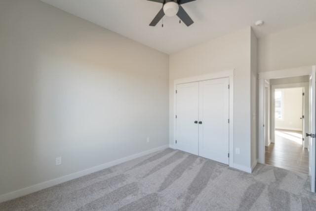 unfurnished bedroom featuring light carpet, ceiling fan, a closet, and baseboards