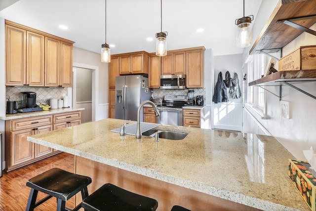 kitchen with a breakfast bar area, a sink, hanging light fixtures, appliances with stainless steel finishes, and light stone countertops