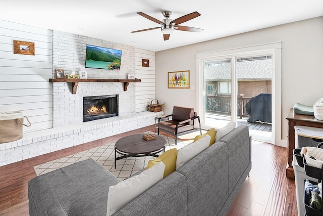 living area featuring a fireplace, a ceiling fan, and wood finished floors