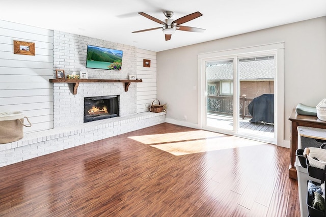 unfurnished living room with ceiling fan, a fireplace, baseboards, and wood finished floors