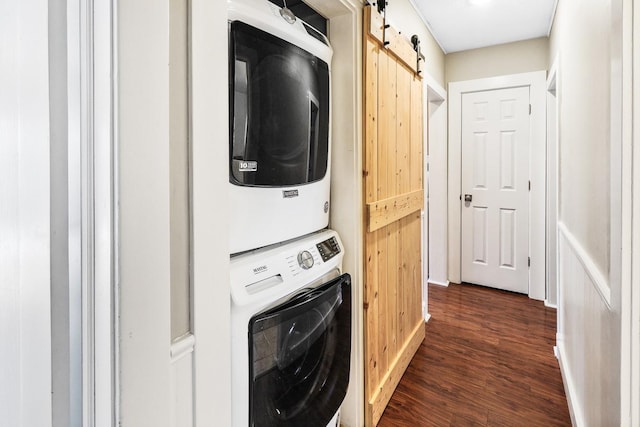 laundry area featuring dark wood-style floors, stacked washer and clothes dryer, a barn door, and laundry area