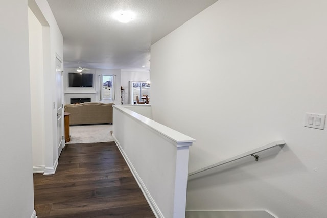 hall with dark wood-style floors, baseboards, a textured ceiling, and an upstairs landing