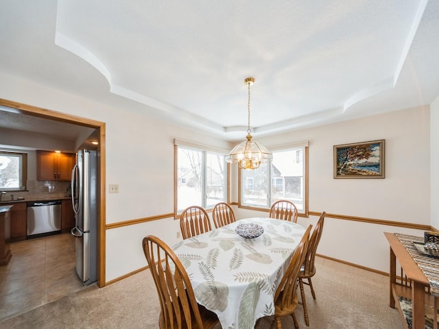 dining space with a raised ceiling, a notable chandelier, a healthy amount of sunlight, and light colored carpet