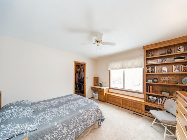 bedroom with a spacious closet, light colored carpet, a closet, and ceiling fan