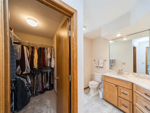 bathroom with vanity, a spacious closet, toilet, and baseboards