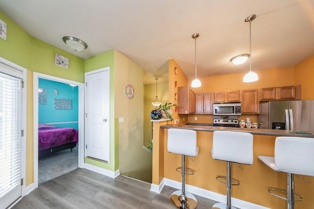 kitchen featuring wood finished floors, a breakfast bar, stainless steel appliances, pendant lighting, and brown cabinets