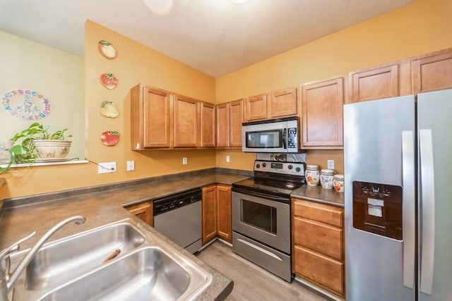 kitchen with a sink, stainless steel appliances, light wood-style floors, and dark countertops