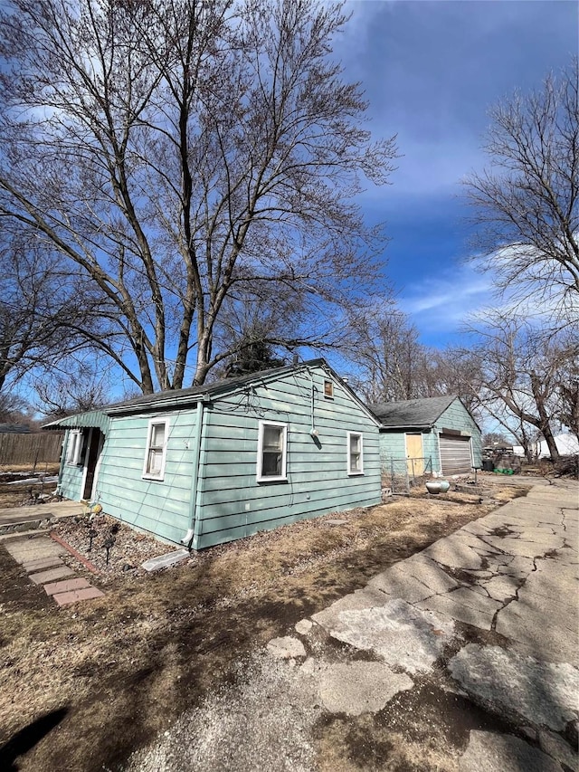 view of side of home featuring a detached garage, driveway, and fence