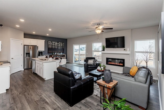 living area featuring a glass covered fireplace, recessed lighting, a ceiling fan, and dark wood-style flooring