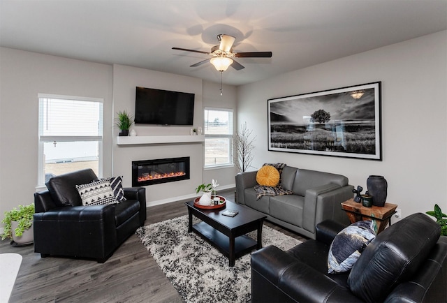 living room featuring a glass covered fireplace, wood finished floors, baseboards, and ceiling fan