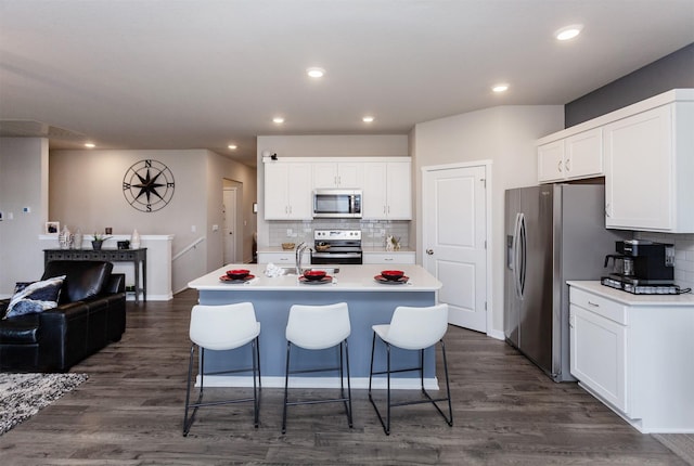 kitchen featuring dark wood-type flooring, a center island with sink, white cabinetry, stainless steel appliances, and light countertops