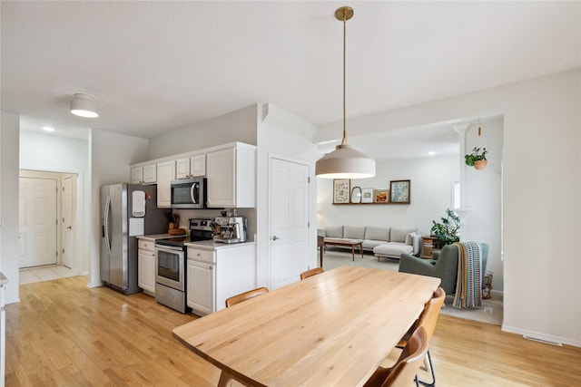 kitchen featuring light wood finished floors, decorative light fixtures, light countertops, stainless steel appliances, and white cabinetry