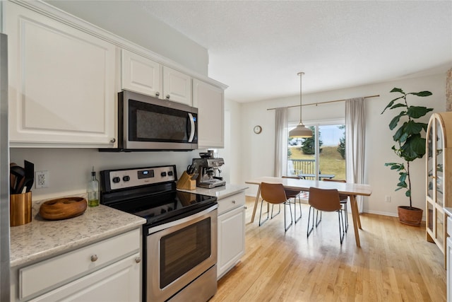 kitchen with pendant lighting, light countertops, light wood-style flooring, stainless steel appliances, and white cabinetry