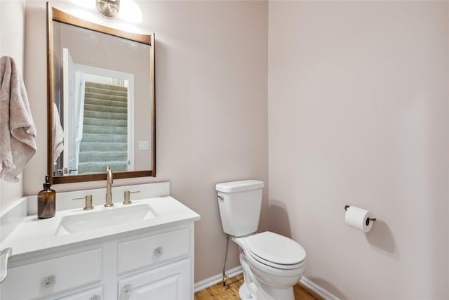 half bath featuring vanity, toilet, wood finished floors, and baseboards