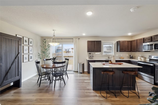 3325 Wolf Creek Rd SW, Bondurant, IA 50035 - kitchen featuring light countertops, light wood-style flooring, a kitchen island, appliances with stainless steel finishes, and dark brown cabinetry