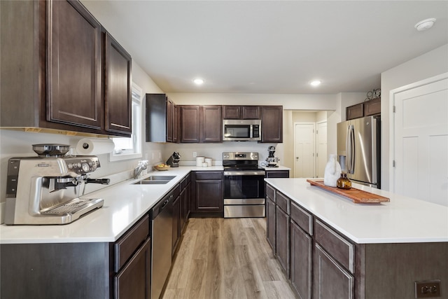 3325 Wolf Creek Rd SW, Bondurant, IA 50035 - kitchen with stainless steel appliances, a center island, a sink, light wood finished floors, and dark brown cabinets