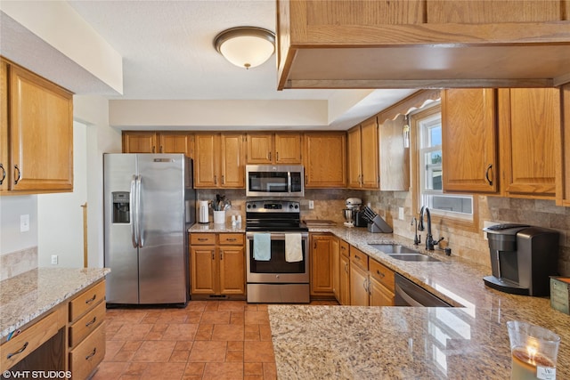 kitchen featuring light stone countertops, a sink, decorative backsplash, appliances with stainless steel finishes, and brown cabinets