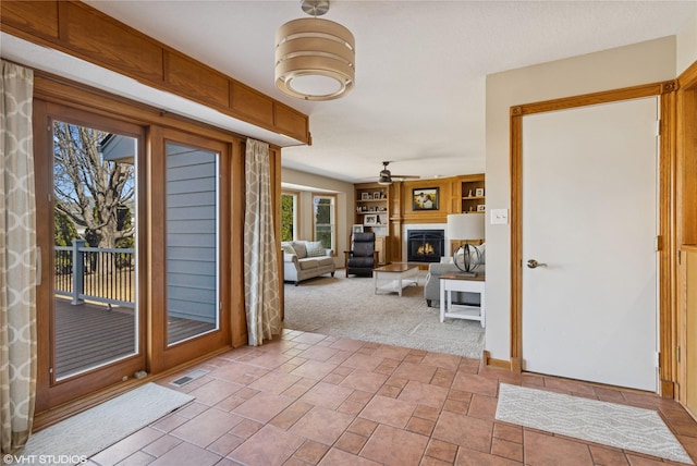 foyer entrance featuring ceiling fan, carpet, visible vents, and a lit fireplace