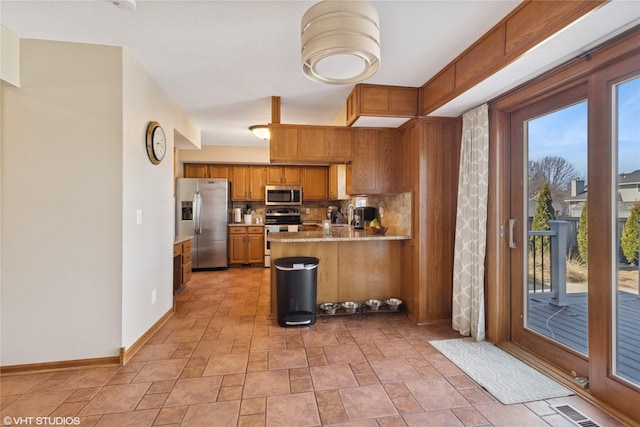 kitchen with a peninsula, plenty of natural light, brown cabinetry, and appliances with stainless steel finishes