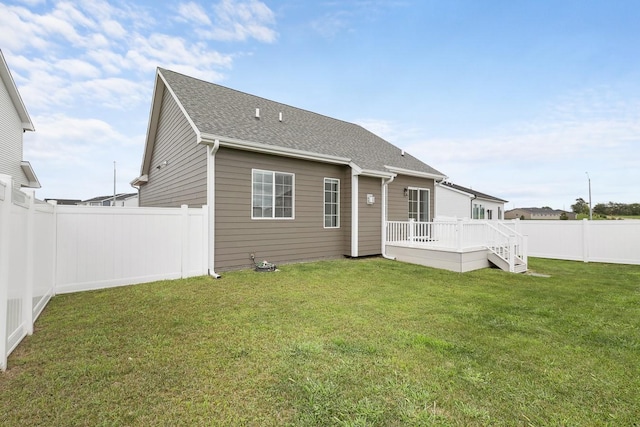 rear view of house with a fenced backyard, a yard, a deck, and roof with shingles