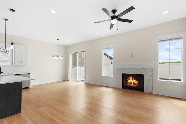 unfurnished living room featuring baseboards, a ceiling fan, light wood-style flooring, and a high end fireplace