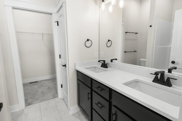 bathroom with double vanity, toilet, a walk in closet, and a sink