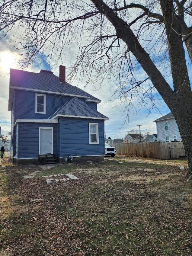 rear view of property with entry steps, a chimney, roof with shingles, and fence