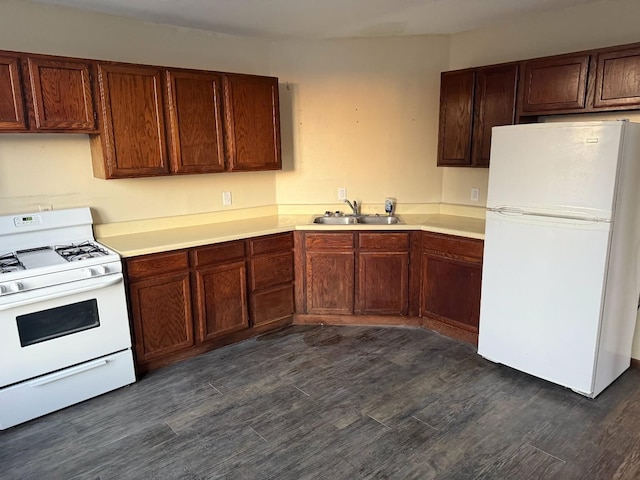 kitchen with a sink, white appliances, dark wood-type flooring, and light countertops