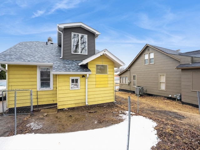 rear view of property with cooling unit, fence, and a shingled roof