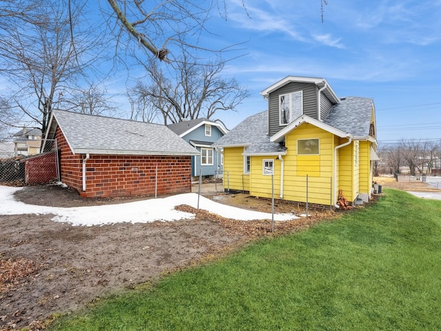 back of property featuring fence, a lawn, and a shingled roof