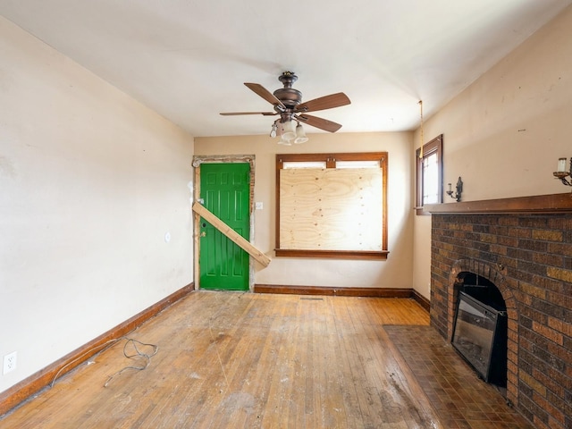 unfurnished living room with a brick fireplace, a ceiling fan, baseboards, and hardwood / wood-style flooring