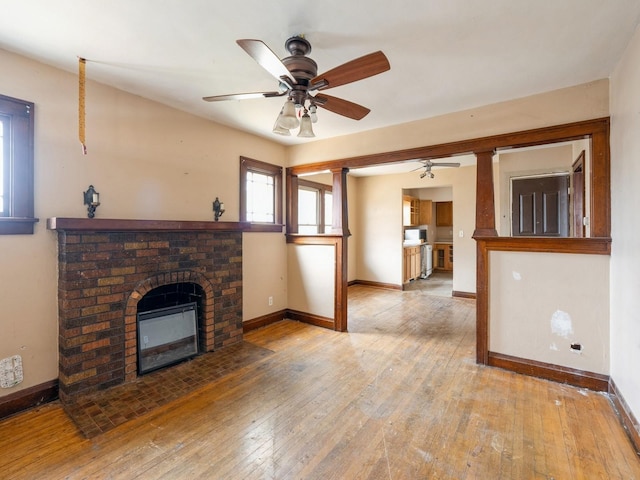 unfurnished living room with a brick fireplace, baseboards, wood-type flooring, and ceiling fan