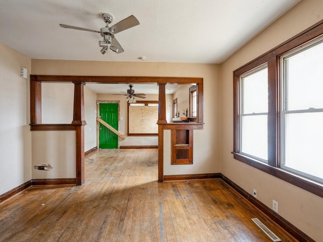 empty room featuring ornate columns, visible vents, baseboards, and hardwood / wood-style flooring