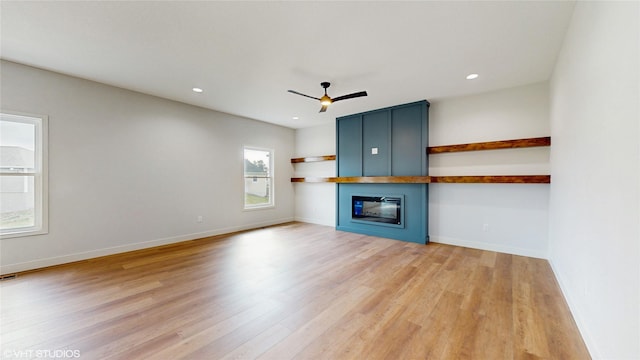 unfurnished living room featuring ceiling fan, baseboards, a fireplace, and light wood-type flooring