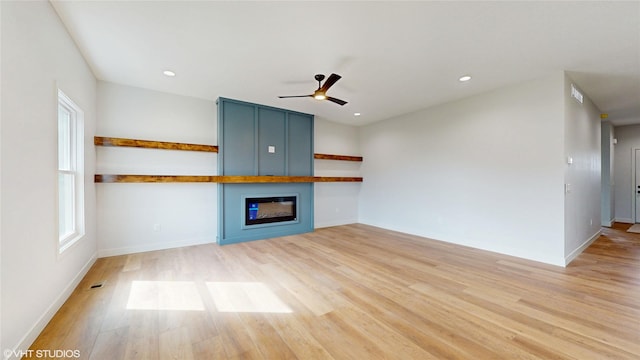 unfurnished living room with recessed lighting, light wood-style flooring, a glass covered fireplace, and a ceiling fan