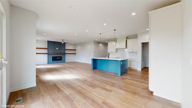 kitchen with a sink, a ceiling fan, a fireplace, a center island with sink, and white cabinets